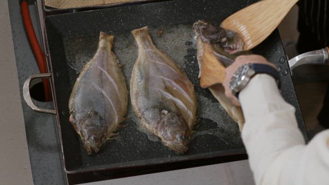 Fish being cooked on a hot pan with oil