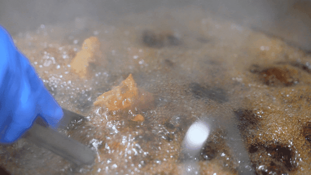 Chicken fried in hot oil with tongs