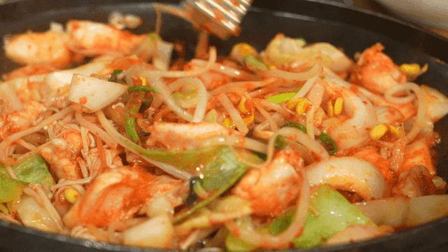 Bokbulgogi being stir-fried with bean sprouts and vegetables in pan with tongs