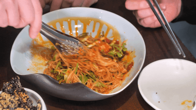 Tongs for mixing spicy whelk salad noodles in bowl