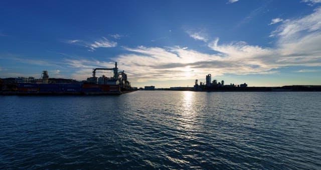 낮부터 저녁까지의 바다 근처에 위치한 산업단지 풍경