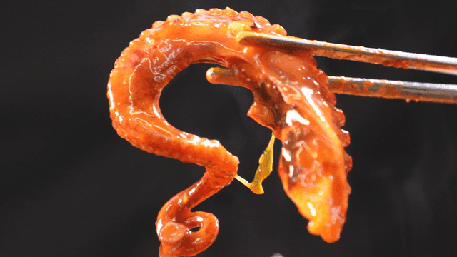 Chopsticks holding octopus leg from spicy seafood stew