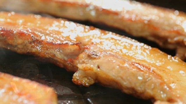 Grilled pork belly sizzling on the pan