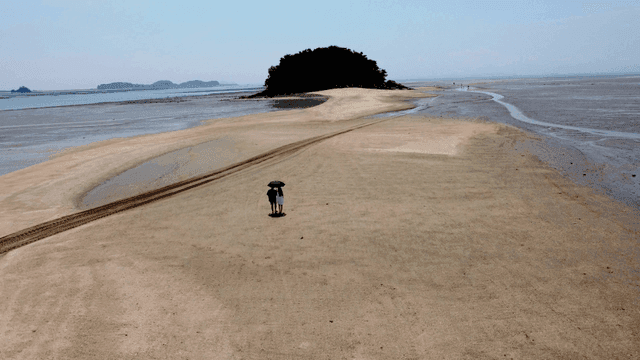 Couple walking with parasols on small island connected by sand