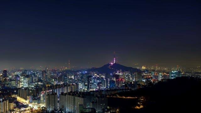 Night view of a bustling cityscape with crescent moon over a mountain tower