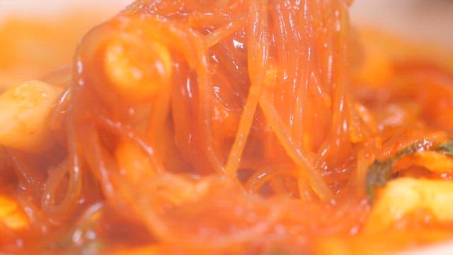 Chopsticks holding glass noodles of spicy tteokbokki