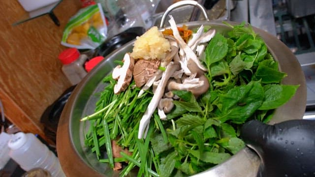 Fresh greens and mushrooms in a metal bowl for hotpot dish