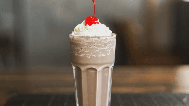 Chocolate milkshake topped with whipped cream and cherries