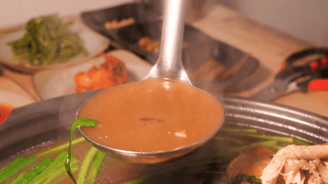 Ladle scooping out rich Samgyetang broth boiling in pot