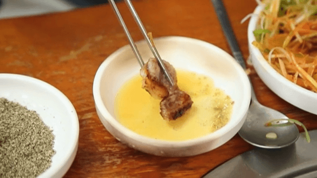 뜨거운 팬 위에서 갓 구운 삼겹살을 참기름장과 들깨가루에 찍기