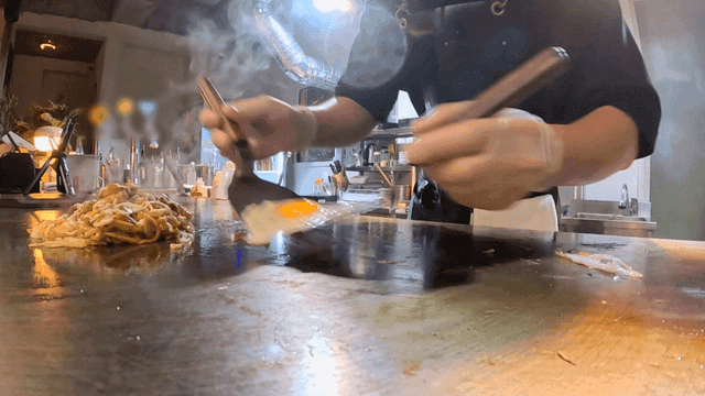 Chef placing fried egg onto griddle yakisoba with spatula