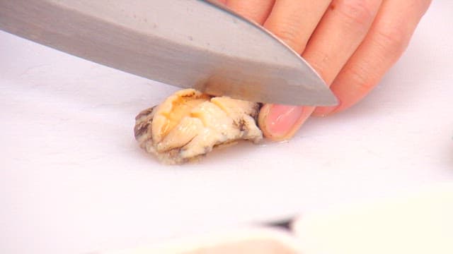 Slicing abalone with a knife on a cutting board