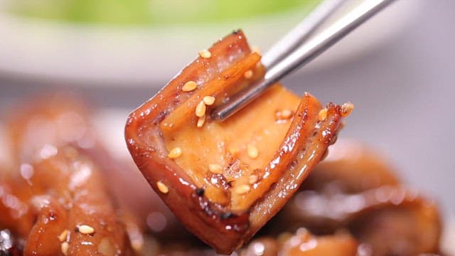 젓가락으로 잡은 윤기 나는 양념 돼지곱창구이