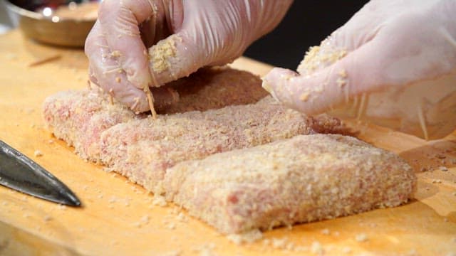 도마 위에서 빵가루를 묻힌 고기를 준비하는 모습