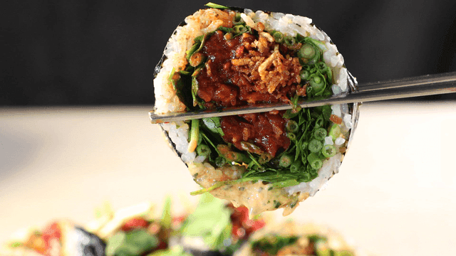 Chopsticks lifting raw beef gimbap filled with fresh vegetables