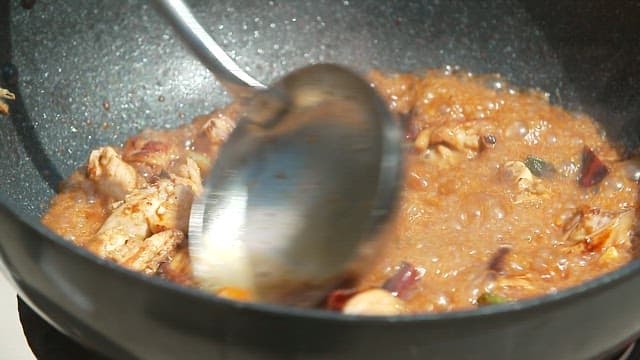 Sauce and meat being stir-fried over high heat in a large wok