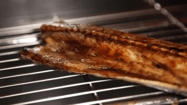 Grilled Spanish mackerel sizzling on metal grill