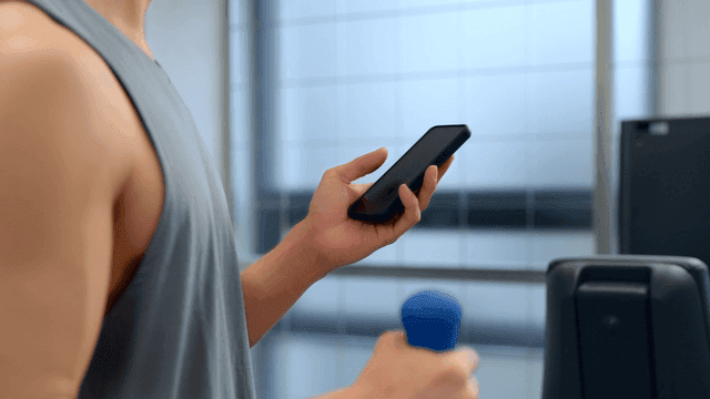 헬스장에서 작은 덤벨을 들며 스마트폰을 사용하는 남성