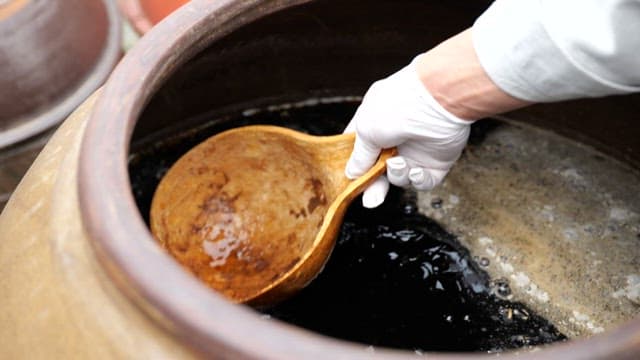 Stirring soy sauce in a crock jar with a wooden ladle