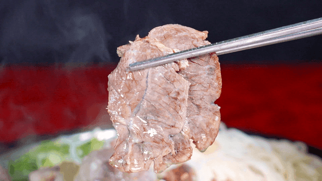Chopsticks holding boiled beef shank from pot