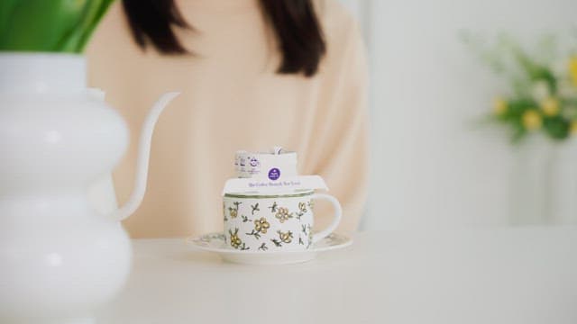 Woman pouring water into cup with coffee pot on table