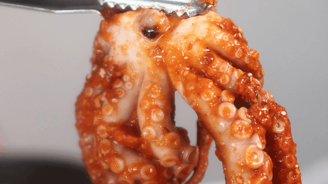 Tongs holding spicy seasoned octopus legs