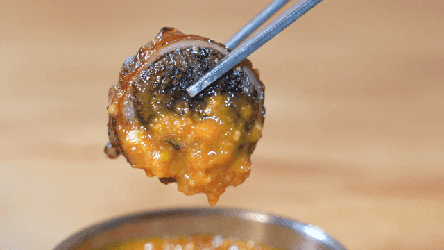 Grilled makchang sundae dipped in soybean paste sauce held by chopsticks