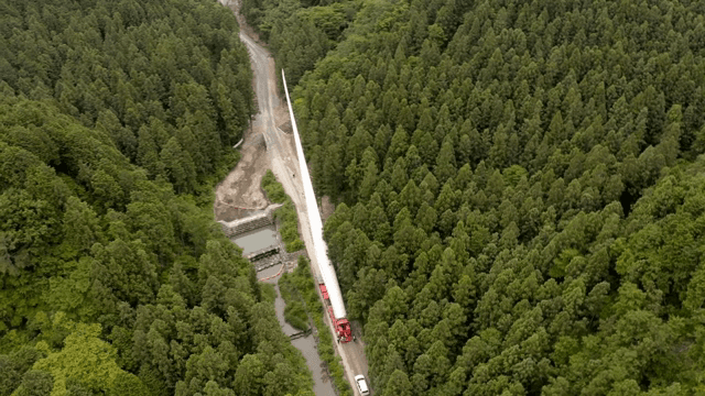 울창한 숲 속 도로에서 풍력 터빈 자재를 운반하는 모습