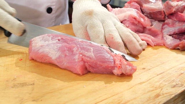 나무 도마 위에서 칼로 생돼지고기 썰기