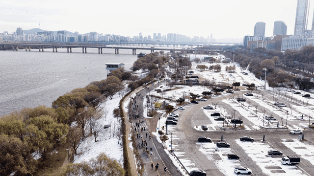 People running in snow-covered riverside park with city view