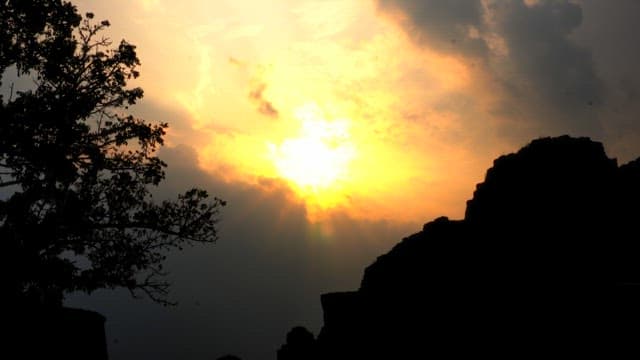 산 실루엣 위 구름 뒤로 해가 지는 풍경