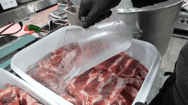 Chef pouring water on raw ribs in kitchen