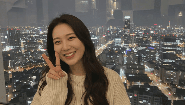 Young woman smiling while facing the night skyline through a tall building window