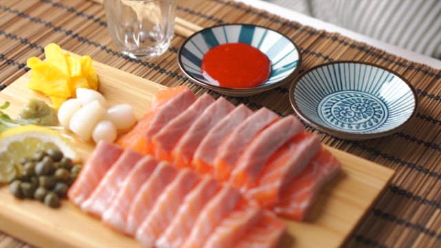 Pouring soy sauce into a bowl next to a wooden cutting board with sliced ​​salmon