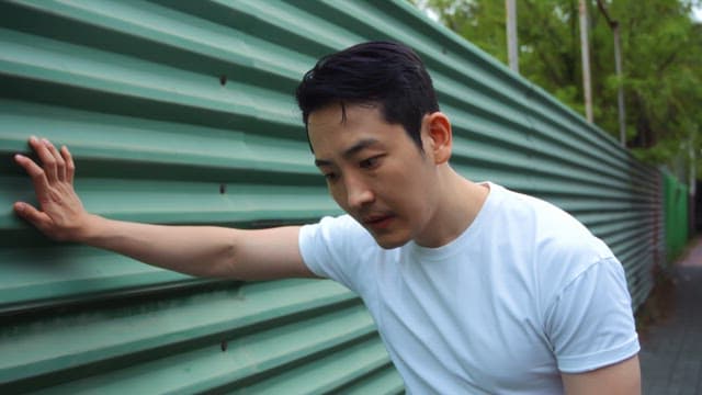 Man leaning against a green wall outdoors