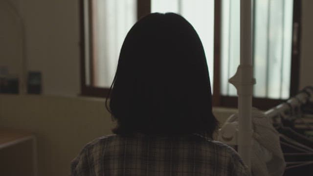 어두운 방에서 창밖을 바라보는 여성