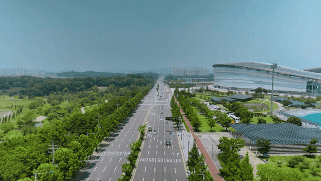 A wide road with surrounding greenery and a stadium