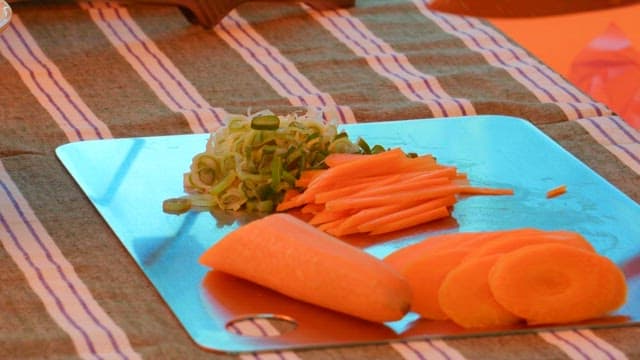 Carrots and green onions being cut with a knife on a small cutting board