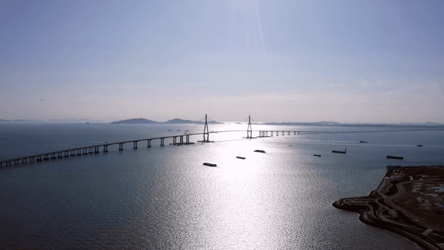 햇빛이 비추는 고요한 바다 위의 긴 다리와 배들
