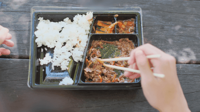 야외에서 한국 도시락을 먹는 사람