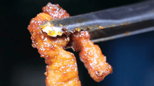 Grilled pork belly held with tongs