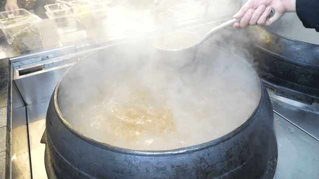 Cook stirring broth with ladle in large pot