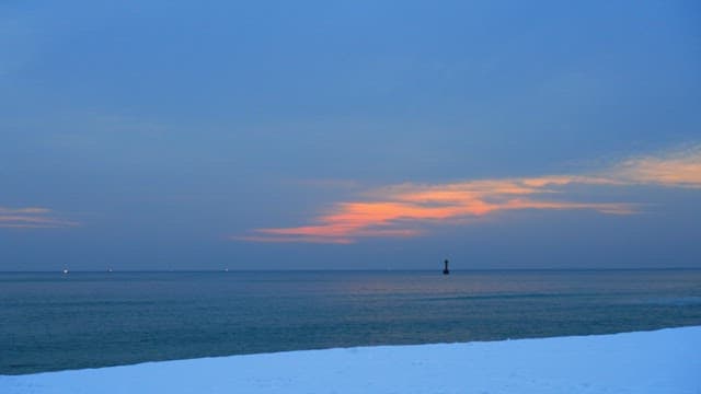 Calm sea and snow-covered beach under the evening sunset sky