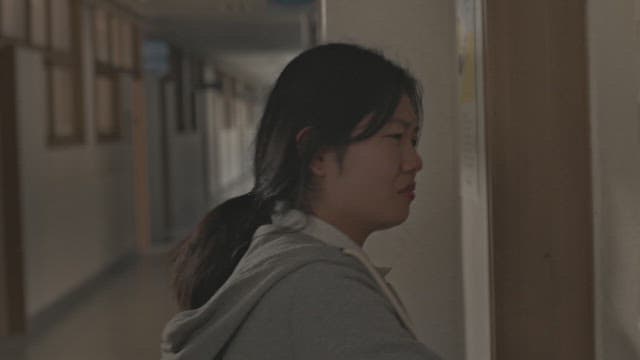 학교 복도에서 문을 바라보며 울먹이는 여학생