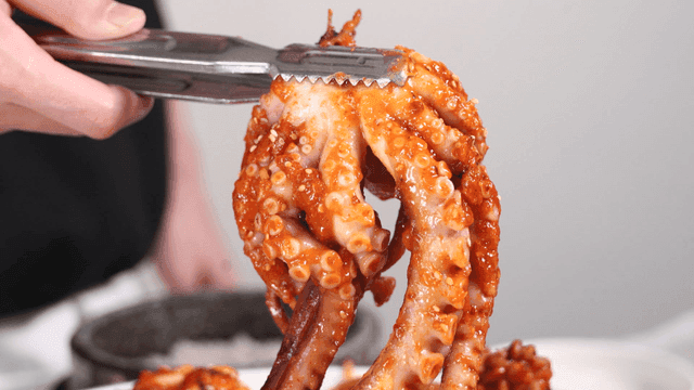 Tongs holding spicy octopus seafood stew