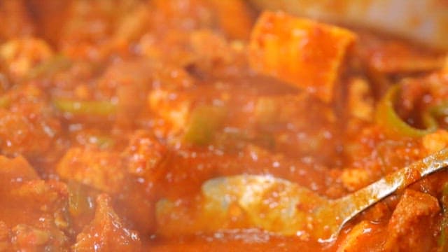 Spoonful of spicy pork stew with plenty of vegetables, tofu, and meat