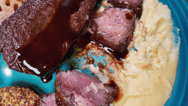 Fork holding juicy steak, mashed potatoes, and vegetables