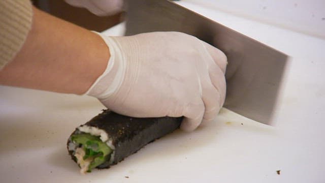장갑 낀 손으로 도마 위에서 맛있는 김밥을 칼로 써는 모습