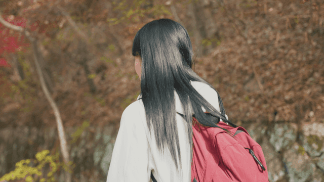 Woman walking through autumn forest with red backpack