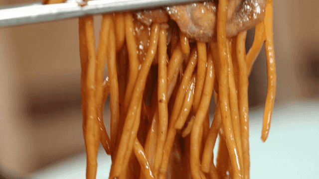 Chopsticks holding noodles and pork